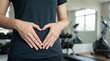 © AlfaSmart - Woman making heart shape with hand on stomach in gym. Healthy lifestyle and fitness concept. Body positivity and care for digestive organ. Active girl training in sports club center.