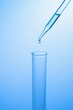 © The Lion Squad - Close up of a glass pipette dropping clear liquid into a laboratory test tube on a blue background