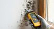 © Nusrat - Person in white glove holding digital moisture meter showing 66.1% humidity on old wall with black mold, indicating water damage and fungal growth.