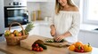 © Hammad - Smiling woman in a white top preparing a healthy meal by slicing a fresh cucumber on a wooden board in a bright modern kitchen with a basket of mixed organic fruits and vegetables.