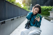 © TeTe Song - Sad young Asian woman sitting outdoors looking at her smartphone, feeling stressed and anxious about bad news, cyberbullying, or relationship problems. Frustrated female reading unhappy text message.