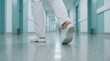 © Wankatsu - Close up view of healthcare professional legs walking in hospital corridor wearing white uniform and professional medical shoes in sterile clinic hallway