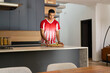 © wavebreak3 - African American man standing at kitchen island holding pizza peel, wearing red jersey and watch