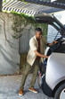 © wavebreak3 - African American man in beige shirt reaching into open white hatchback under slatted pergola