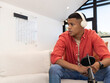 © wavebreak3 - Adult man sitting on sofa in modern living room wearing headphones and recording with microphone