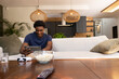 © wavebreak3 - African American man sitting in living room holding tablet wearing navy t-shirt popcorn on table