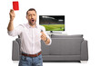 © Ljupco Smokovski - Man watching a football game at home and holding a red card and a whistle