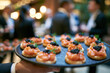© Olga Ко - Garçom servindo canapés finos em evento corporativo de networking com executivos ao fundo desfocado