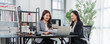 © Kritdanai - Lawyer Consultation: Two women in professional attire are having a consultation, possibly legal, in a modern office setting with a laptop and paperwork on the desk.