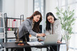 © Kritdanai - Legal Consultation: Two professional women, one a lawyer, review documents and a laptop in a modern office, discussing a case with focus and diligence, implying legal advice and strategy.