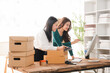 © Kritdanai - Startup Success: Two female entrepreneurs are diligently working on their new venture, organizing packages and reviewing data on a computer in a bright and airy workspace.