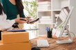 © Kritdanai - Warehouse Operations: Two women are diligently working in a warehouse setting, one using a calculator and the other pointing at it. They are surrounded by shipping boxes and office equipment.