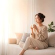 © jidapa - young woman sitting on a sofa and drinking coffee