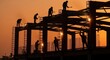 © Tuklu - Silhuetas de operários da construção civil na estrutura de um prédio contra o céu do pôr do sol.
