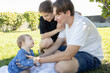 © Anna - Happy young parents and their baby spend time in the park sitting on the grass. A loving family of three enjoys time together. Lifestyle. Family day