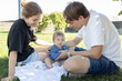 © Anna - Happy young parents spend time in the park with their little daughter, sitting on the grass and admiring her. A loving family of three of European descent enjoys together. Lifestyle. Family day
