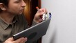 © Aliaksandr - Professional electrician connecting electrical wires to a new wall socket, utilizing a digital tablet for reference or smart home integration during renovation and installation