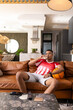 © wavebreak3 - Man sitting on brown sofa in living-room wearing red jersey, holding basketball and sipping glass