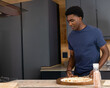 © wavebreak3 - African-American man in navy tee preparing pizza on board at counter with pink grinder, copy space