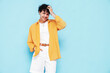 © halayalex - Young attractive man with short curly hair hairstyle. Smiling handsome male in casual stylish yellow shirt and shorts clothes posing in studio, isolated on blue. Cheerful and happy model
