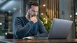 © firdol - Focused Businessman Thinking While Working Late on Laptop in Modern Office