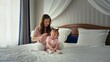 © MIKHAIL - Mother gently brushes her young daughter's hair while they sit on a cozy bed in pajamas, sharing a tender, peaceful morning routine of care, bonding and sweet smiles at home