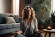 © SADEWA - Middle aged woman meditating at home with eyes closed, relaxing body and mind in a living room