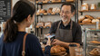 © Pakpong - Smiling barista serving customer using mobile payment at bakery counter with fresh pastry