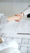 © rogerphoto - Handshaking between two architects finalizing a construction project deal, business partners agreeing on engineering blueprints and architectural models in an office, close up