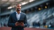 © Adi - Confident businessman holding tablet at outdoor sports stadium