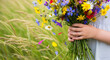 © Iryna - Small child hands holding colorful wildflower bunch in summer meadow with tall grass, childhood innocence and nature connection