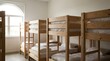 © geny - Bunk beds in a dormitory room with a large arched window. The wooden beds are neatly made with white linens