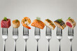© akhsan - A line of forks, each holding a different piece of seafood, including tuna, scallop, shrimp, salmon, cod, and mackerel, presented against a plain background