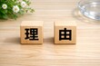 © Jumpei - 木の机に置かれた理由という漢字が書かれた積み木と白い花とガラスの皿がある無人の風景