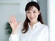 © Jumpei - 白いシャツを着て室内で笑顔で手を振り挨拶をする清潔感のある若い女性の上半身写真