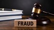 © emwe studio - Wooden block with fraud text in front of legal judge gavel and stacked books on desk