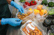 © CoreRock - Careful worker wearing blue glove on hand sorting fresh vegetable food into plastic packaging on metal table for hygienic preparation and safe grocery delivery