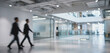 © Vhagar - Two business professionals walking through a modern office space with blurred background, showcasing a collaborative workplace environment.