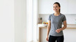 © Xenia - Smiling fit woman standing in a bright modern kitchen. Happy athletic female in sportswear. Healthy lifestyle and fast metabolism concept