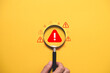 © Dilok - Warning alert concept with magnifying glass focusing on danger symbol over yellow background. Risk management, security monitoring, problem detection, caution and safety awareness concept.
