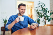 © baranq - Man smiling at smartphone with coffee at home dining table