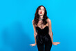 © deagreez - Woman in black strapless top blowing a kiss against a bright blue background, glamorous pose with red lips and wavy brunette hair