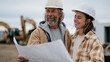 © forenna - Older general contractor handing over blueprints and client keys to his daughter at a job site trailer, succession planning moment between parent and adult child, construction equipment parked outsi