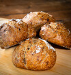© Julien - Four classic farm country bread buns stacked on a wooden chopping board. These homemade rustic rolls balls are made of organic wholemeal multigrain wheat flour for a sourdough recipe.