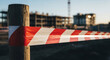 © ViskBx - Red and white hazard warning tape wrapped around a wooden post at a construction site with blurred building structures in the background