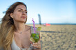 © SISMIZ - Woman enjoying a refreshing cocktail on a sunny beach with the ocean in the background