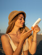 © SISMIZ - Woman applying sunscreen on beach at sunset with straw hat and bikini