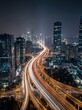 © SOEM - A long-exposure photograph captures a sprawling cityscape at night. A multi-level highway dominates the foreground, its lanes filled with streaks of light from passing vehicles.