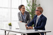 © David - Businesswoman collaborating with a senior businessman, discussing financial analytics on a laptop, working together on a project in a modern office, developing new strategies