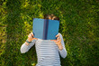 © Westend61 - Girl lying on meadow reading a book